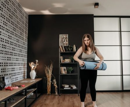 Plus size woman rolling a yoga mat in a stylish indoor setting with modern decor.