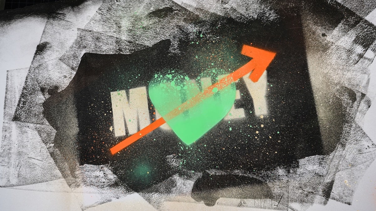 Urbane Collage-Kunst auf Papier: Eine expressive Street-Art-Kombination aus dem geschablonenhaften Wort "MONEY", einem zentralen, gesprühten, neon-grünen Herzen und einem diagonalen, orangefarbenen Pfeil, der nach oben zeigt. Die rohe, schwarz-weiße Hintergrundstruktur und die Farbspritzer erzeugen einen dynamischen, urbanen Vibe. Das Bild symbolisiert das komplexe, aber oft positive Verhältnis von Erfolg und Leidenschaft.